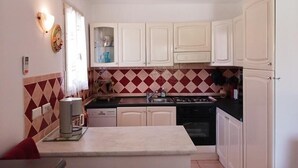Une cuisine compacte avec des meubles blancs, un crédence rouge et beige, un lave-vaisselle encastré et une cuisinière à gaz.