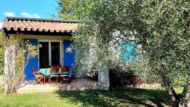 Une petite maison avec un toit en tuiles, une façade bleue et une terrasse avec une table et des chaises.