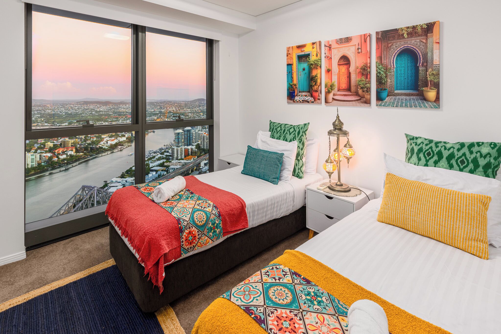Un dormitorio con un ventanal grande, una cama, una mesita de noche y vistas a un paisaje urbano.