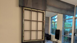 Een modern interieur met een groot raam, een zwarte metalen scheiding en een zwarte bureaustoel.