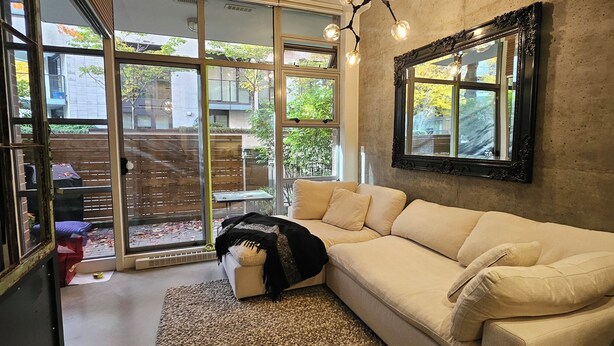 Een moderne woonkamer met een beige bank, een getextureerd vloerkleed en een groot raam met uitzicht op de omgeving.
