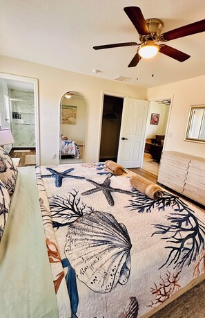 A bedroom with a bed, a ceiling fan, a door, and a hallway.