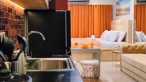 A modern kitchen with a stove, sink, and orange cookware. A dining area with a sofa and a chandelier is visible in the background. - Reminisce Staycation  (Pasay)