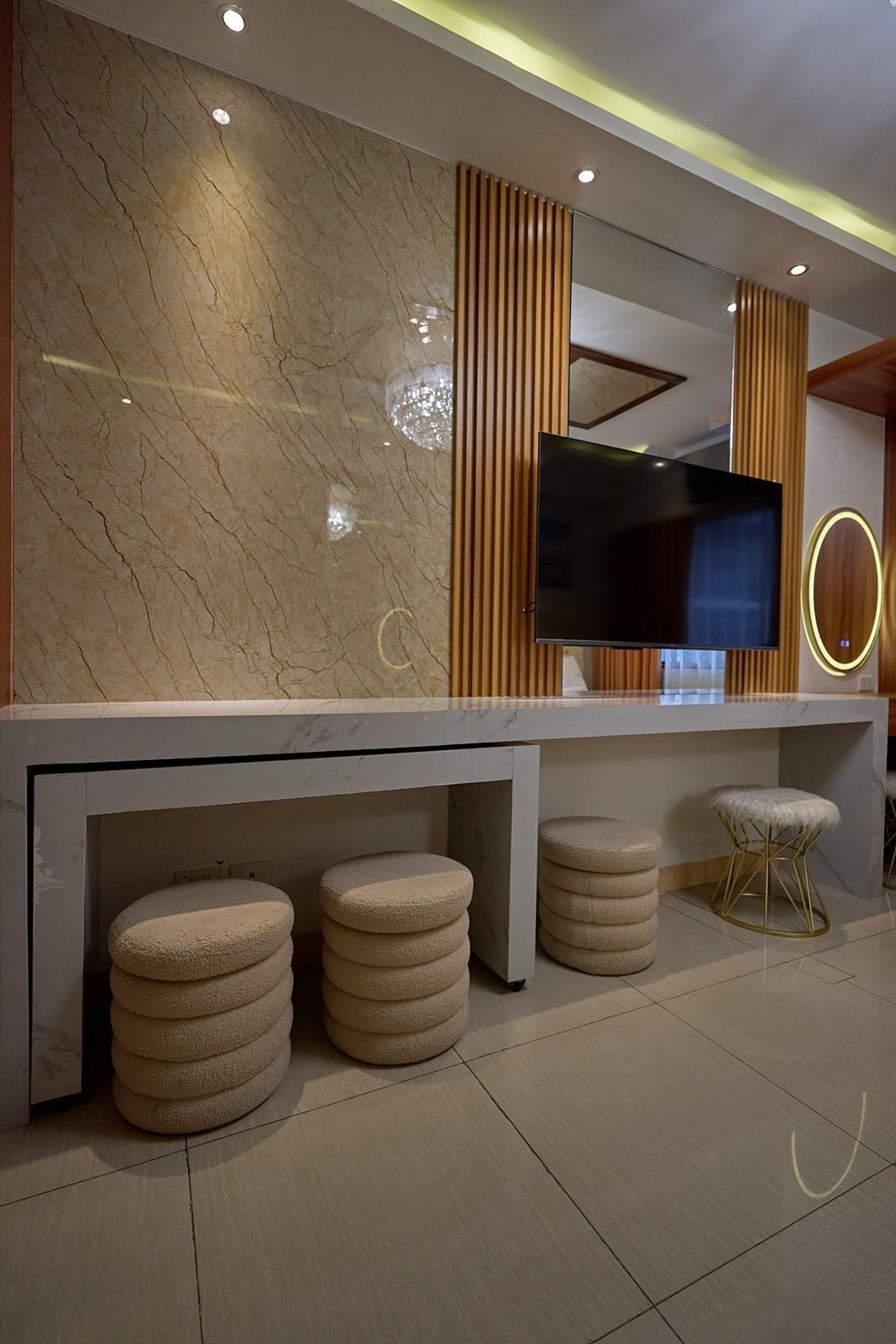 A modern living room with a marble wall, a flat-screen TV, wooden panel accents, and round ottomans.