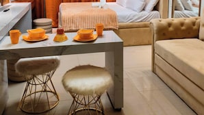 A modern hotel room with a bed, a sofa, a dining table with orange dishes, and a chandelier. - Reminisce Staycation  (Pasay)