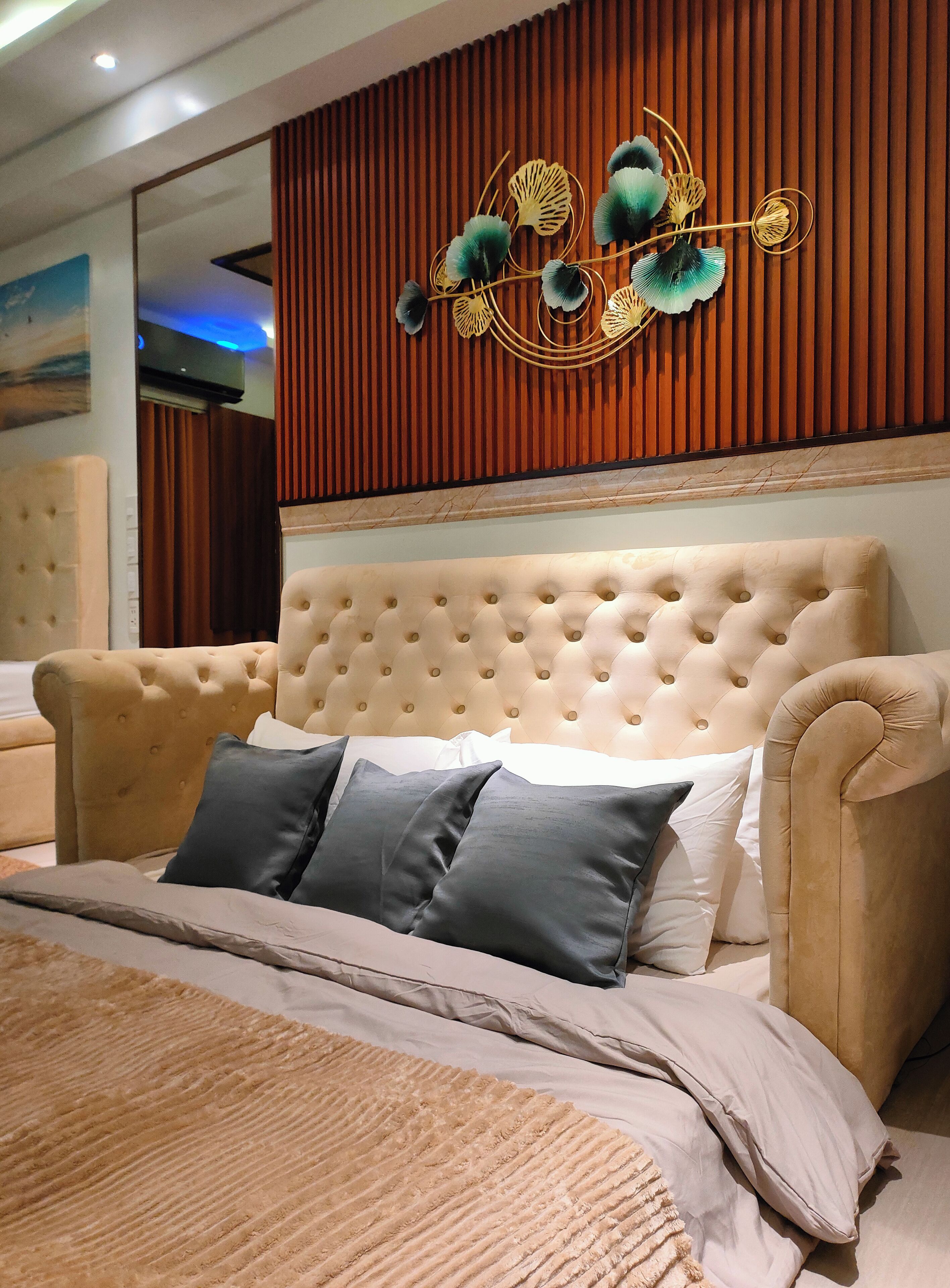A bedroom with a tufted headboard, a large bed with multiple pillows, and a decorative wall piece above the bed.