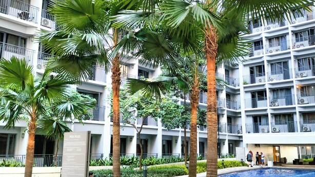 A modern building with multiple balconies, a swimming pool, and palm trees. - Reminisce Staycation  (Pasay)