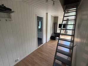 Um corredor com painéis brancos, piso de madeira, uma escada preta e uma porta de acesso a um banheiro.