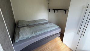 Una habitación pequeña con una cama, un estante y un armario.