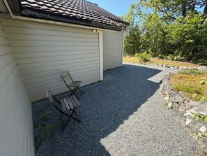 A covered outdoor area with a gravel path, a folding chair, and a building with a tiled roof.