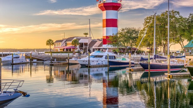 Un port de plaisance avec des bateaux amarrés, un phare et un bâtiment avec un toit rouge.