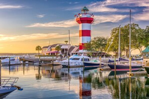 A marina with boats docked, a lighthouse, and a building with a red roof. - NEW LISTING!! Cane & Current ~ 6 Marsh Dr ~ Luxury 6BR Sea Pines Home w/ Pool, Spa & Fire Pit (Hilton Head Island)