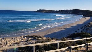 A coastal beach with a wooden walkway leading to the shore, rocky terrain, and a clear view of the ocean. - Cuttlefish Bay Cottage | Australia View | Luxury (Cuttlefish Bay)