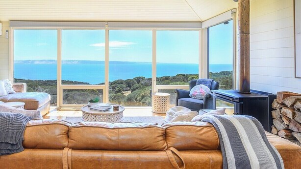 A cozy living room with a leather sofa, a fireplace, and a large window offering a view of the ocean. - Cuttlefish Bay Cottage | Australia View | Luxury (Cuttlefish Bay)