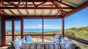 A wooden deck with a cushioned seating area overlooking a scenic landscape. - Cuttlefish Bay Cottage | Australia View | Luxury (Cuttlefish Bay)