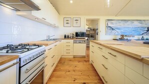 A modern kitchen with white cabinets, a wooden countertop, and a stove. There is a painting of a coastal scene on the wall. - Cuttlefish Bay Cottage | Australia View | Luxury (Cuttlefish Bay)