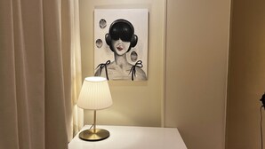 Une table de chevet avec une lampe, un tableau encadré accroché au mur et un rideau à moitié tiré.