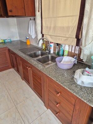 A kitchen with granite countertops, wooden cabinets, a stainless steel sink, and various cleaning supplies.