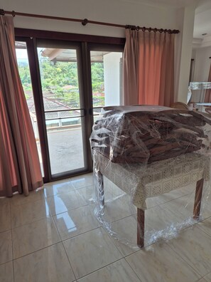 A room with a bed covered in protective plastic, a sliding glass door leading to an outdoor area, and a view of greenery outside.