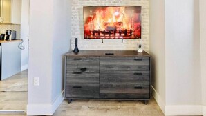 Een moderne woonkamer met een open haard, een flatscreen televisie erboven en een donker houten kast eronder.