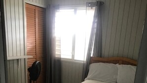 Een slaapkamer met een bed, een ventilator, een raam met gordijnen en een deur.