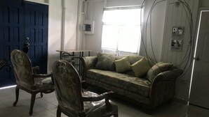 A living room with a sofa, two chairs, a table, a blue door, and a window. - Enjoyable 2nd story, 3-bedroom house with AC in Coamo, PR (Coamo)
