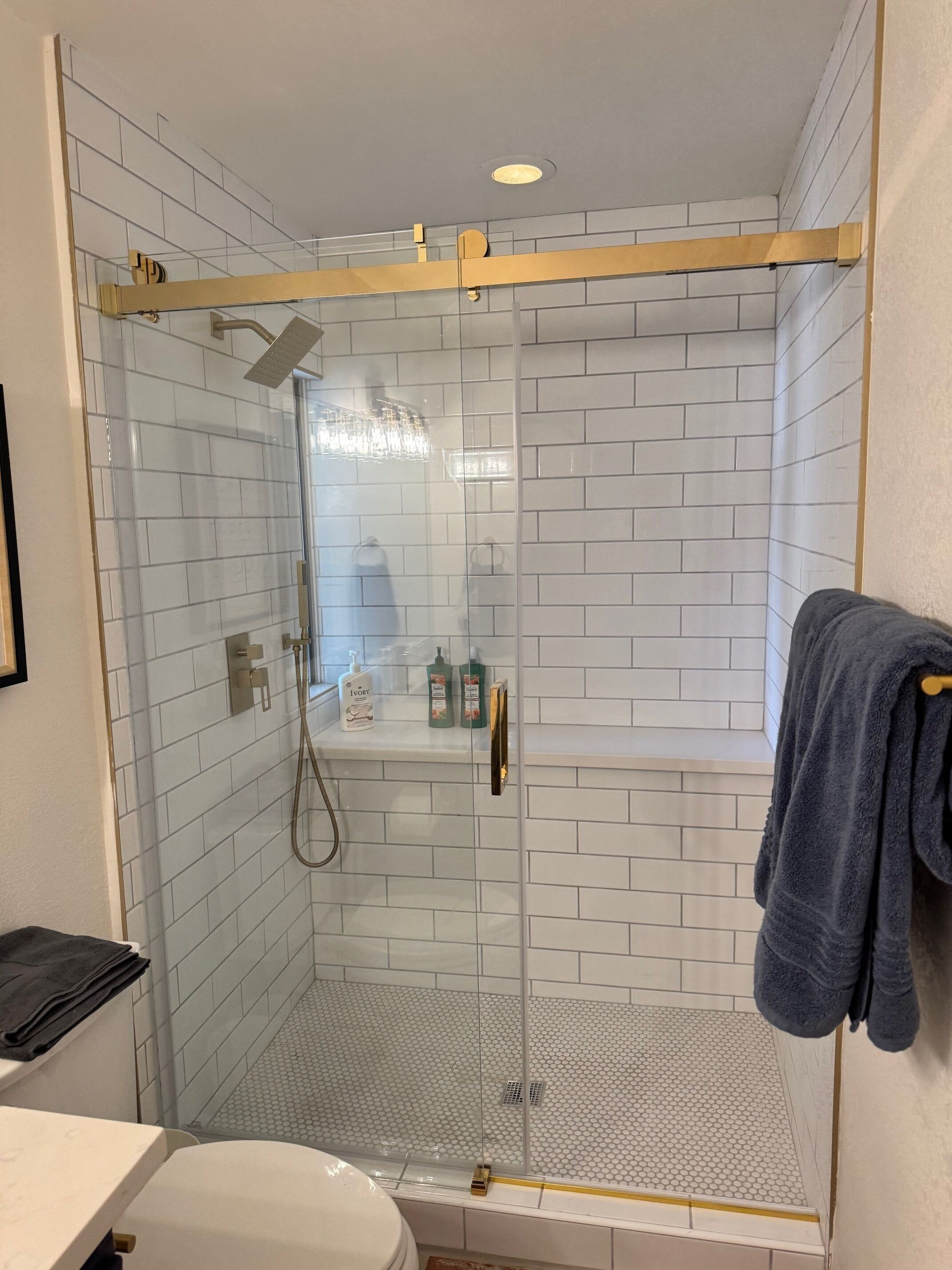 A glass-enclosed shower with white tiled walls and a wooden shelf above.