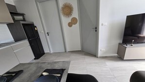 A modern kitchen with a dining area, a TV, and a door with decorative wall art. - Modern Retreat 1- Bed T3-529 (Chalong)