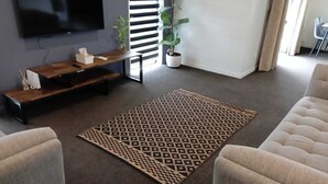 A modern living room with a flat-screen TV mounted on the wall, a wooden entertainment unit, a patterned rug, and a potted plant.