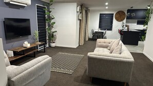 A modern living room with a grey sofa, a flat-screen TV, and a dining area with a table and chairs.