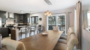 A modern kitchen with dark cabinets, a wooden dining table, and a hanging light fixture.