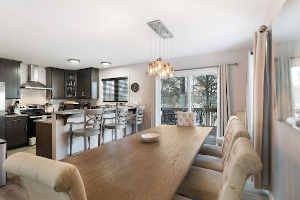 A modern kitchen with dark cabinets, a wooden dining table, and a hanging light fixture.