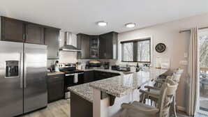 A modern kitchen with dark cabinets, stainless steel appliances, a granite countertop, and a large island with bar stools.