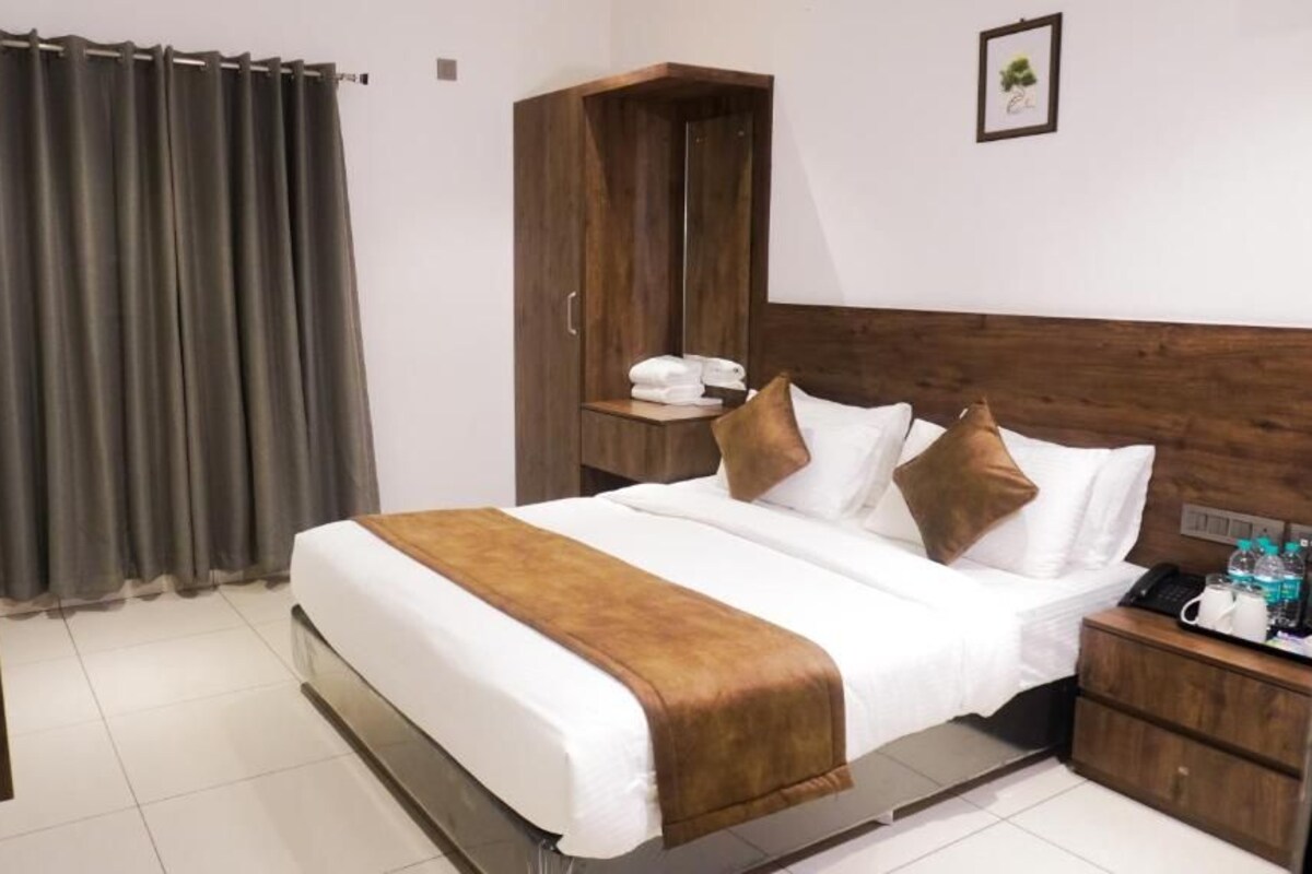 A hotel room with a large bed, a wooden wardrobe, a bedside table with a phone and toiletries, and a curtain.