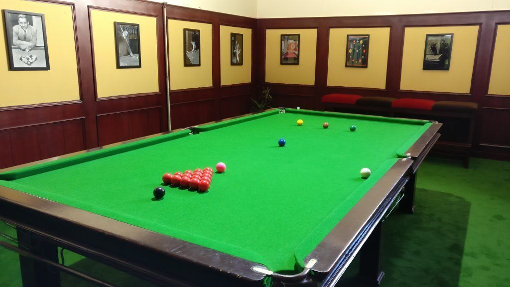 Een pooltafel met ballen, ingelijste foto's aan de muur en een rode, beklede bank.