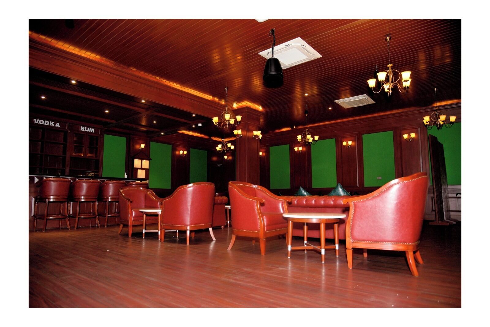 A bar area with leather chairs, wooden bar counters, and green screens.