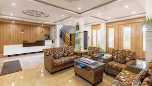 A reception area with a wooden reception desk, brown patterned sofas, a glass coffee table, and a staircase in the background. - Young Monk Hostel Dharamkot (Dharamshala)