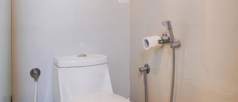 A bathroom with a toilet, a shower, and a trash bin.