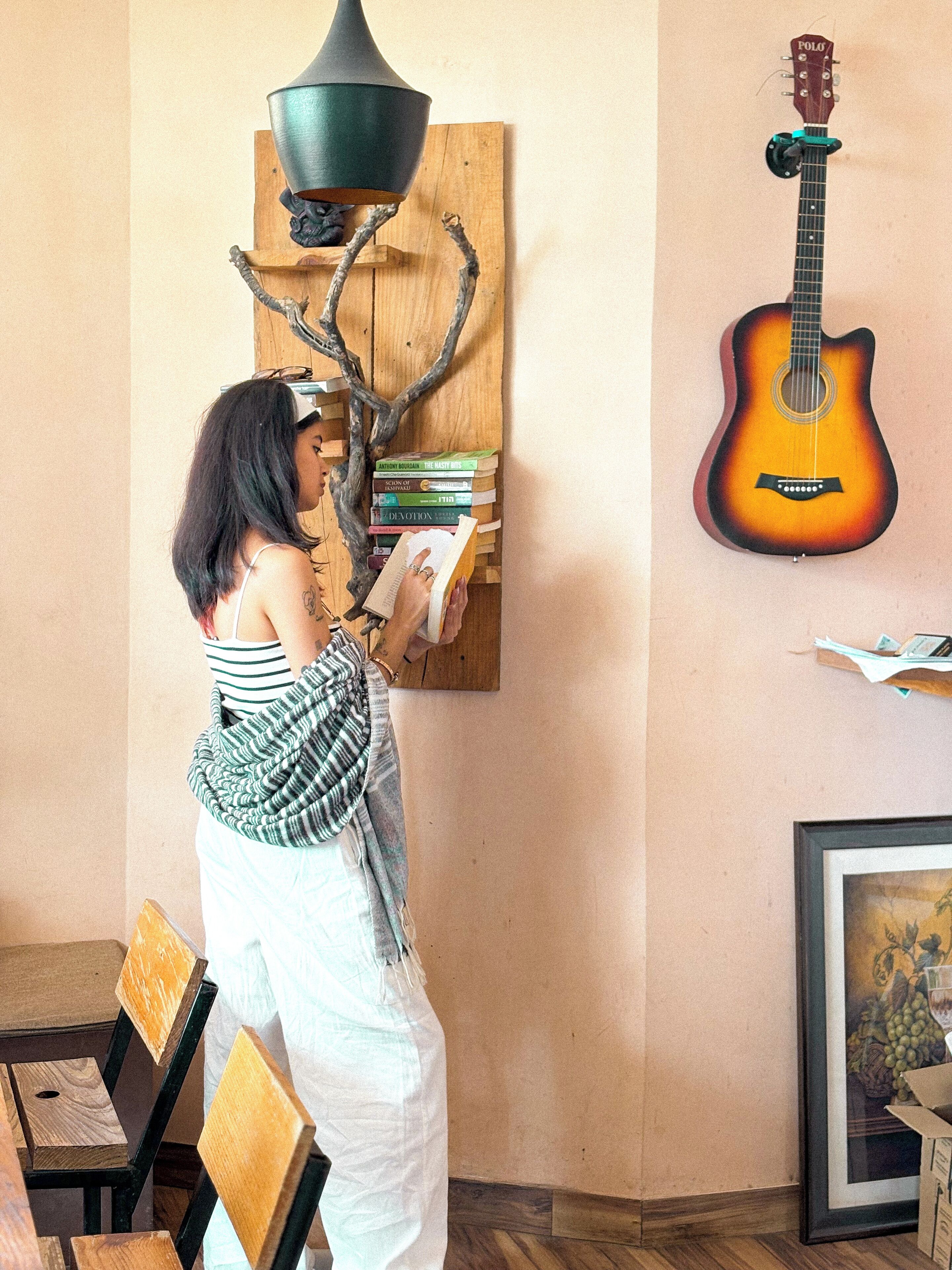 Una habitación con un estante de madera que contiene libros, una guitarra y una lámpara colgante.