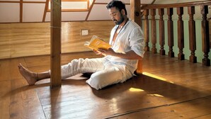 A person sitting on the floor in a room with wooden beams and a slanted ceiling, reading a book. - Young Monk Hostel Dharamkot (Dharamshala)