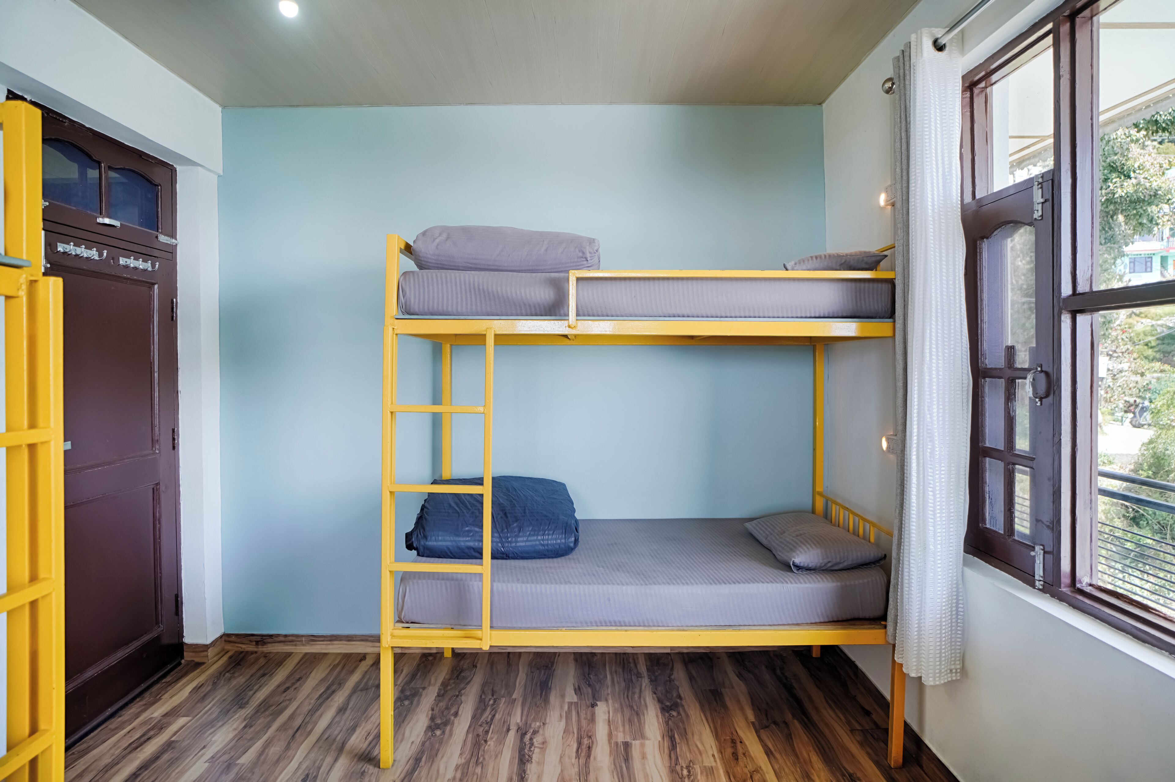 A bunk bed room with a wooden ladder, a wardrobe, and a window with a view.