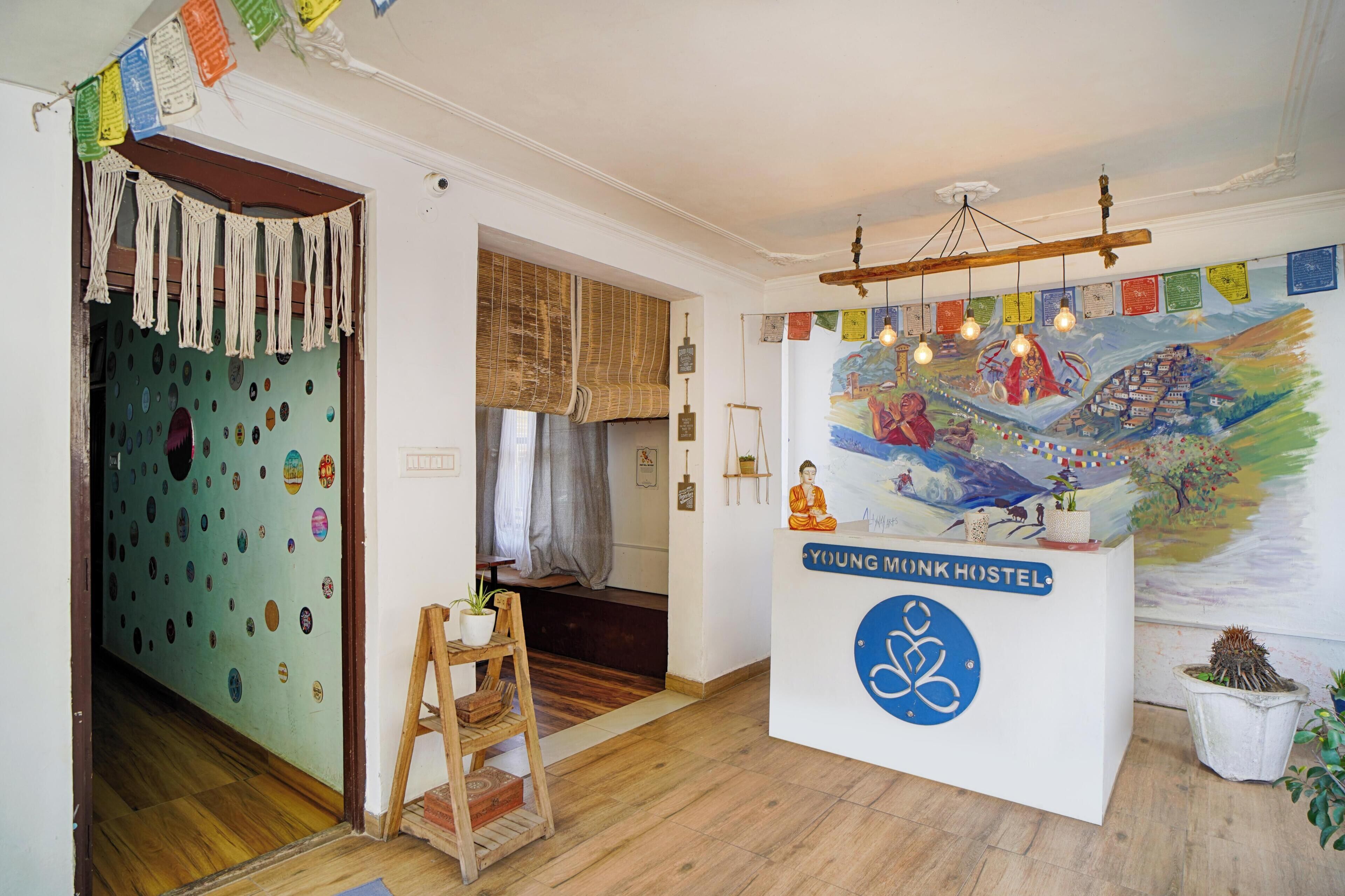 Une pièce avec un plancher en bois, une statue de Bouddha, un mur décoré de motifs colorés et une enseigne indiquant l’auberge de jeunesse « Young Monk ».