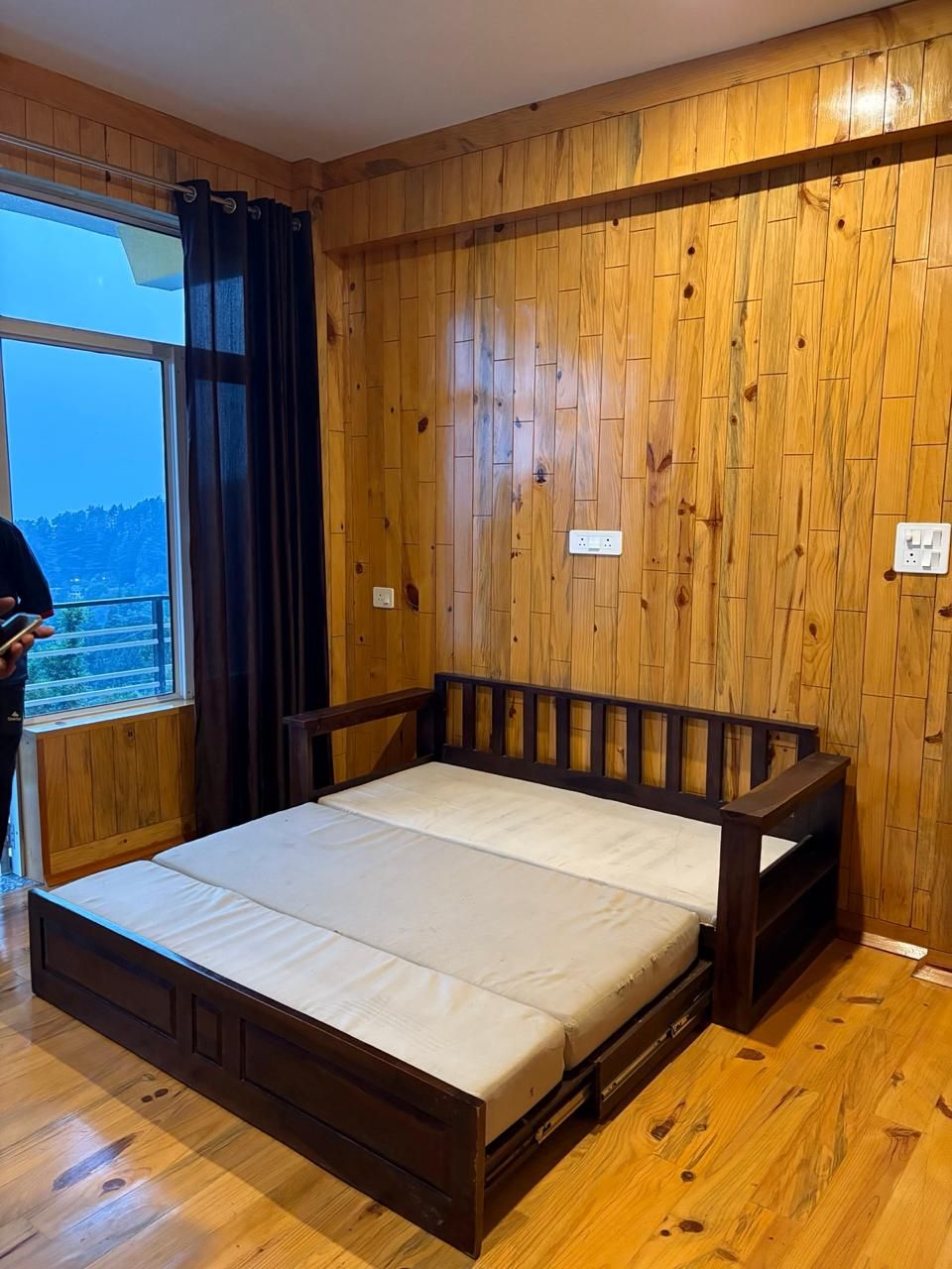 Een slaapkamer met een houten vloer, een bed met houten frame en een raam met gordijnen.
