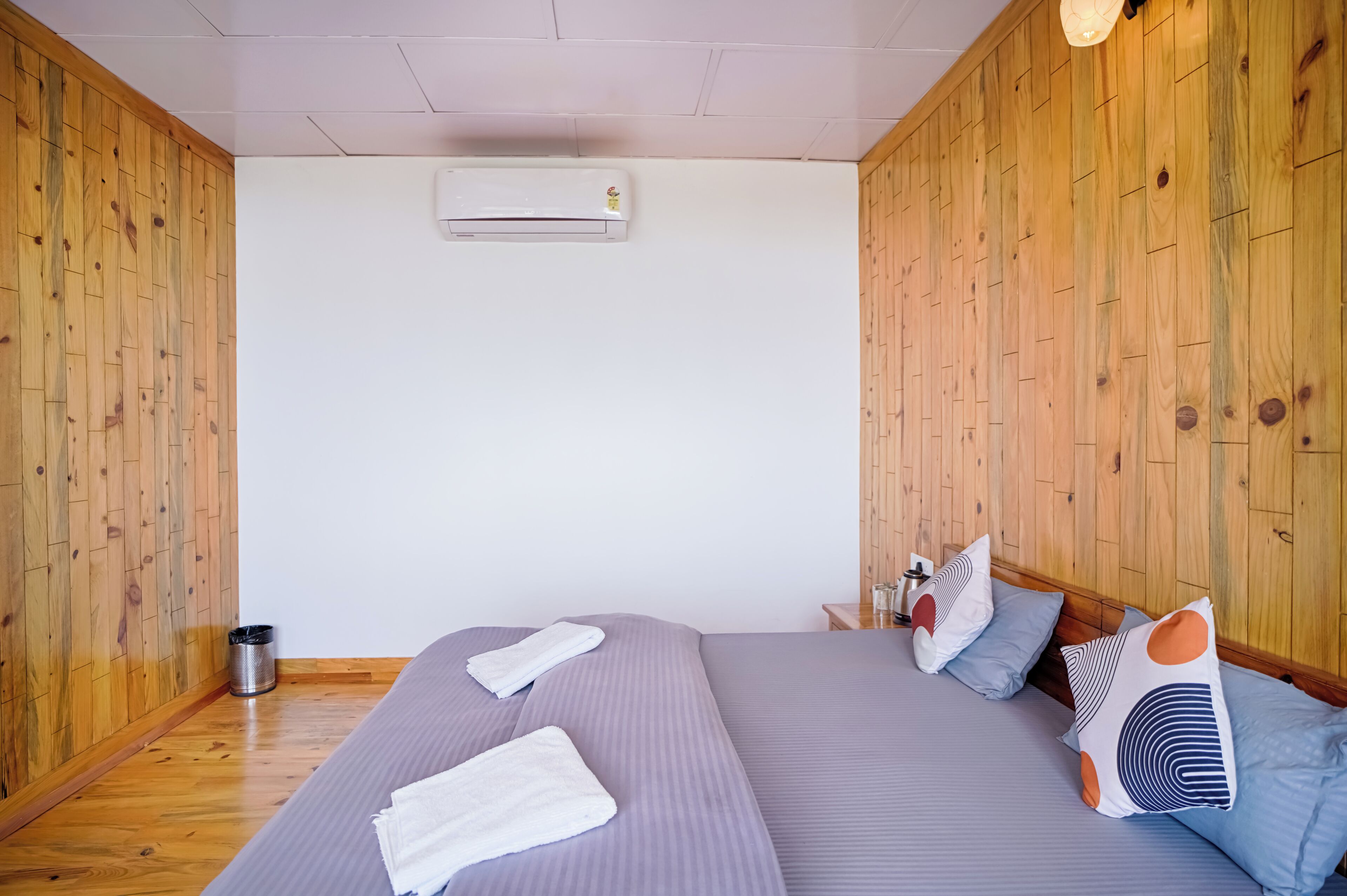 A bedroom with a wooden paneled wall, a bed with grey bedding, white towels, and decorative pillows.