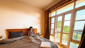 A bedroom with a large bed, wooden headboard, and a view through a sliding glass door. - Young Monk Hostel Dharamkot (Dharamshala)
