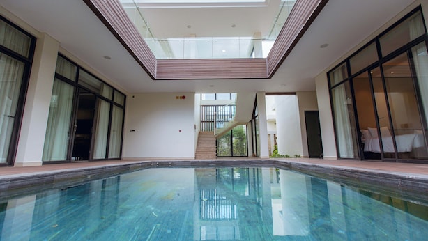 Une piscine dotée d’un toit en verre, de grandes fenêtres et d’un escalier menant à un niveau supérieur.