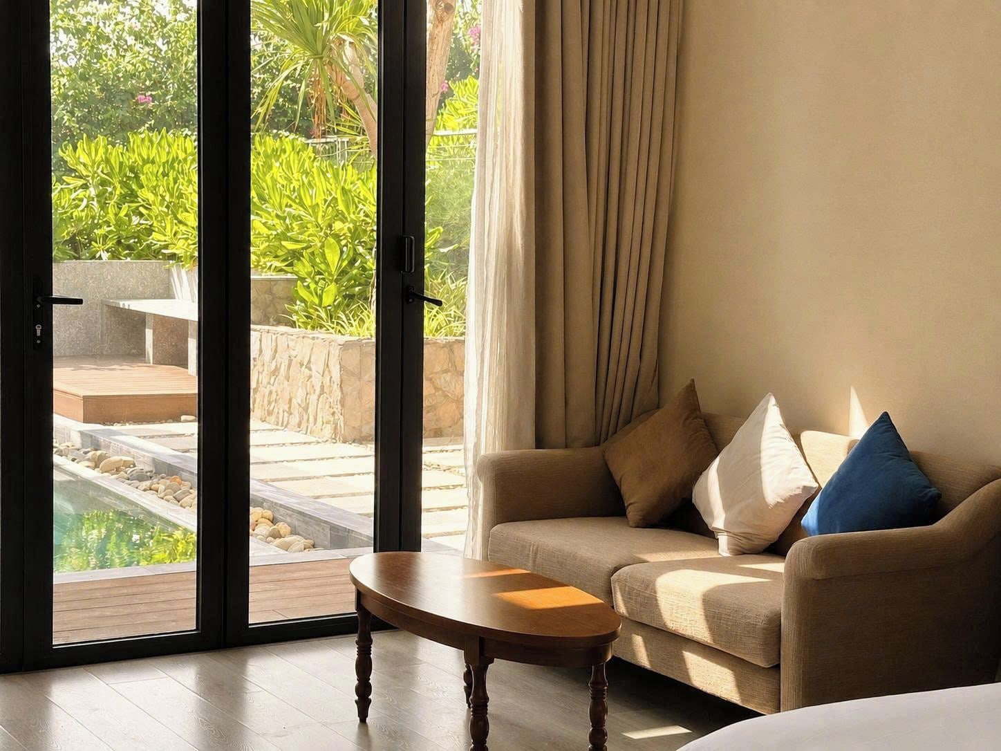 Una habitación con sofá, una mesita y vistas a un espacio exterior con plantas y una fuente.
