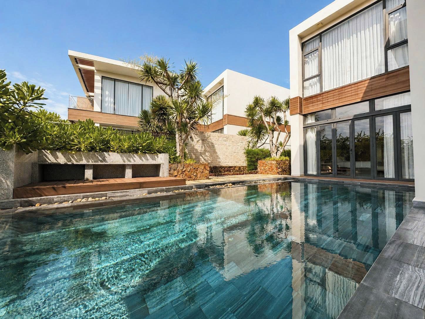 A modern residential pool area with a clear pool, surrounding plants, and a stone wall.