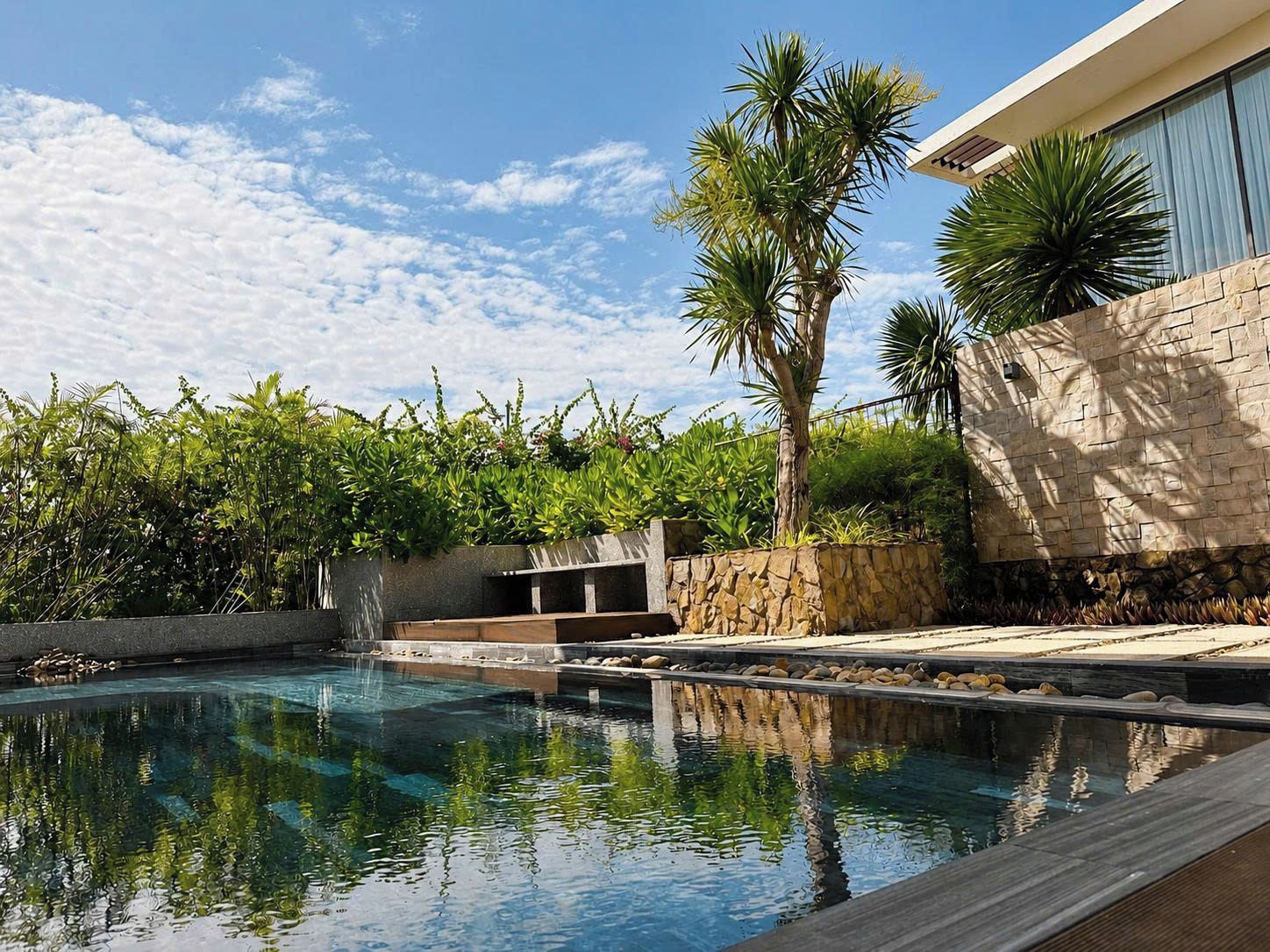 A swimming pool with a stone wall and palm trees.