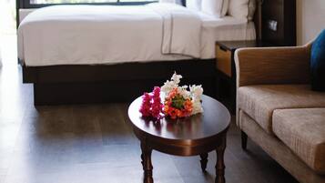 Quarto de hotel com uma cama, um sofá, uma mesa redonda de madeira com flores e uma janela grande com cortinas.